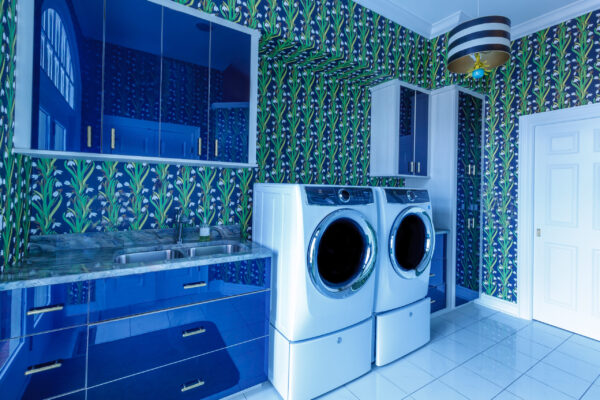 Vibrant laundry room with blue cabinets, marble counters, white washer/dryer, & floral wallpaper.