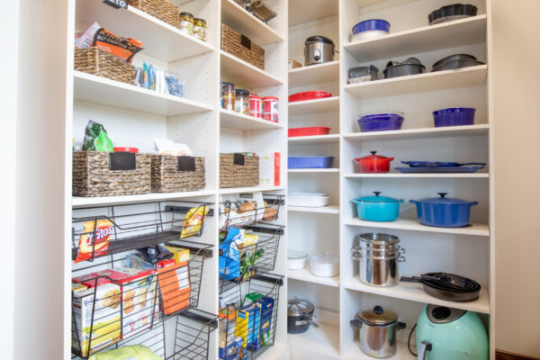 Organized pantry with white shelves, wicker baskets, wire pull-out drawers, cooking tools, and small kitchen appliances.