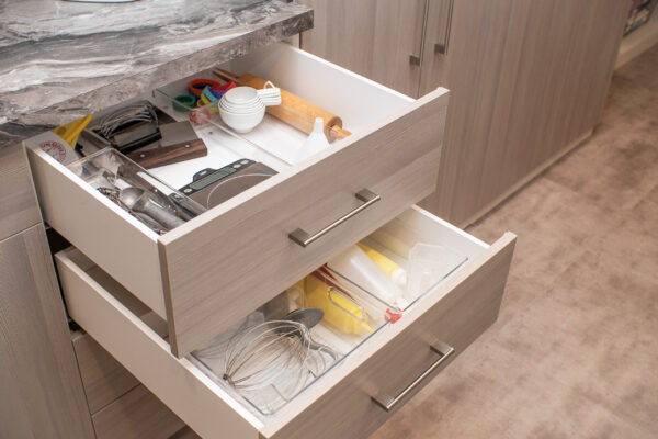 Open kitchen drawers with baking tools, including a rolling pin, measuring cups, and a whisk.