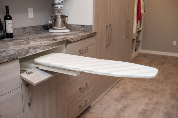 Built-in pull-out ironing board from a light wood drawer with dark gray marble counter and KitchenAid mixer.