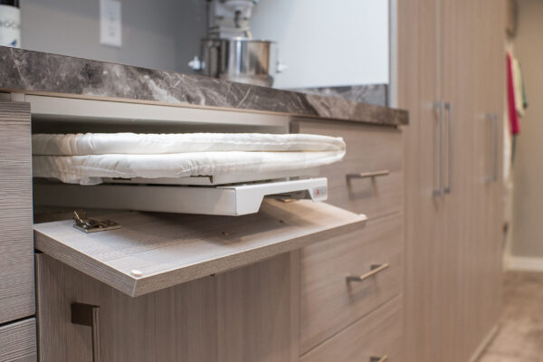 A folded white ironing board pulled out from a cabinet drawer, with a dark marble countertop above.