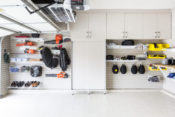 Garage with light gray cabinets, slatwall organization, and white epoxy flooring. Sports gear, tools, and golf bags are neatly stored.