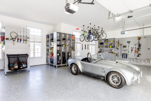 A bright and organized two-car garage with a silver gray Shelby Cobra parked on a gray speckled floor.
