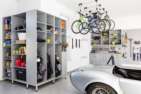 Organized garage with gray storage cabinets, wall panels, overhead bike racks, and a silver sports car.
