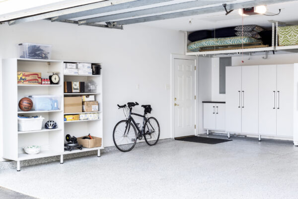 Organized white garage with storage cabinets, overhead racks, a bicycle, and epoxy flooring.