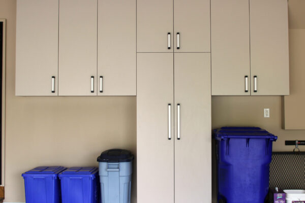 Light brown garage cabinetry with silver hardware, two blue recycling bins, one gray trash can, and a large blue wheeled bin.