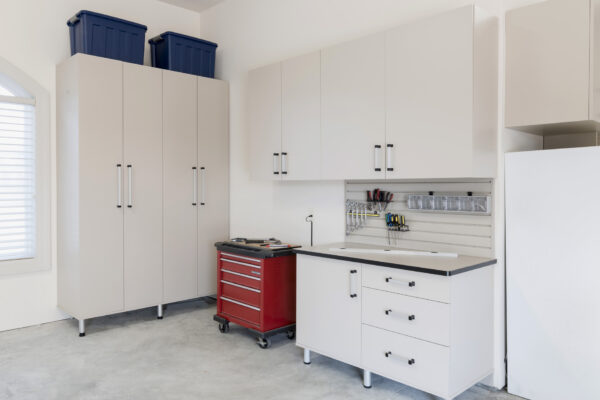 Organized garage workshop with light gray cabinets, red tool chest, workbench, and wall-mounted tools.