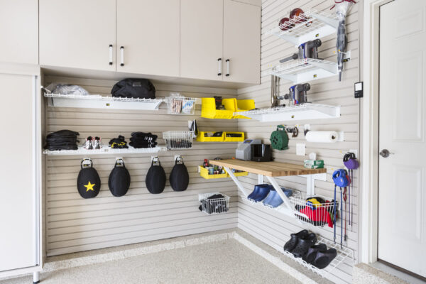 Organized garage with light gray slatwall, shelving, yellow bins, tools, a workbench, and a white door.