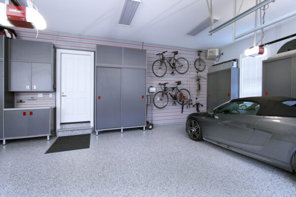 Gray garage with car lift, custom cabinets, slatwall with bikes, epoxy flooring, and white door.