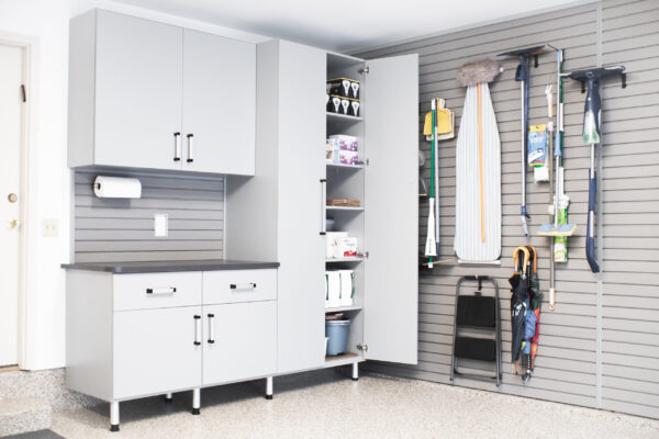 Light gray garage cabinets with black handles, slotted wall organization for cleaning supplies, and a speckled floor.