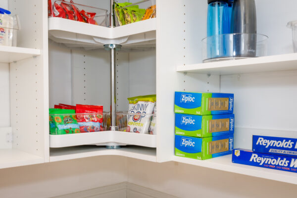 White pantry corner with 2-tier lazy Susan full of fruit snacks & chips, Ziploc bags, and aluminum foil.