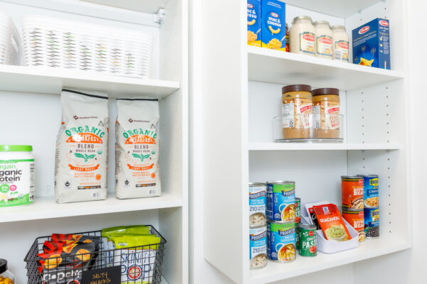 Organized white pantry shelves with coffee, protein powder, pasta, peanut butter, and canned goods.