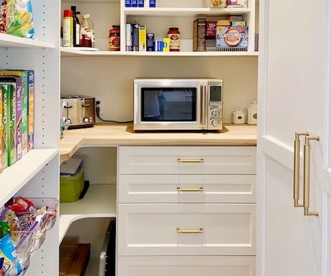 Spacious pantry with white shelves, drawers, and a microwave on light wood counter.