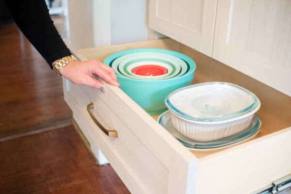 Woman opens kitchen drawer with turquoise nesting bowls and glass bakeware.