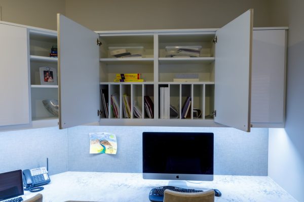 Built-in white office cabinets above a desk with computer, phone, and papers.