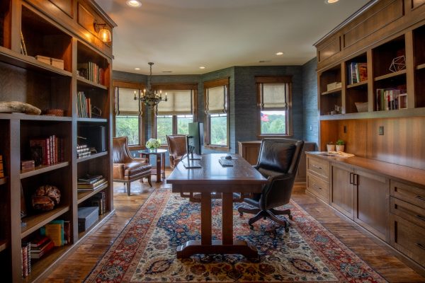 Cozy home office with built-in dark wood bookshelves, a large desk, and a colorful rug.