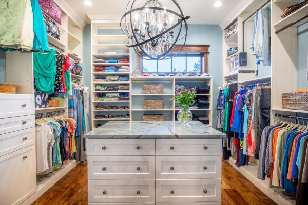 Spacious walk-in closet with white shelving, light blue walls, and a large central island with a marble top.