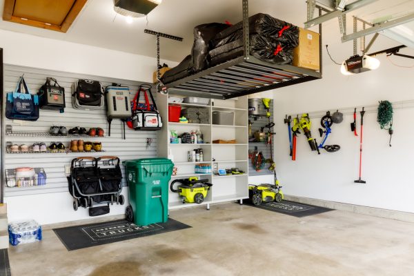 Organized garage with slatwall, ceiling storage, shelves, and various tools, mops, and bags hanging.