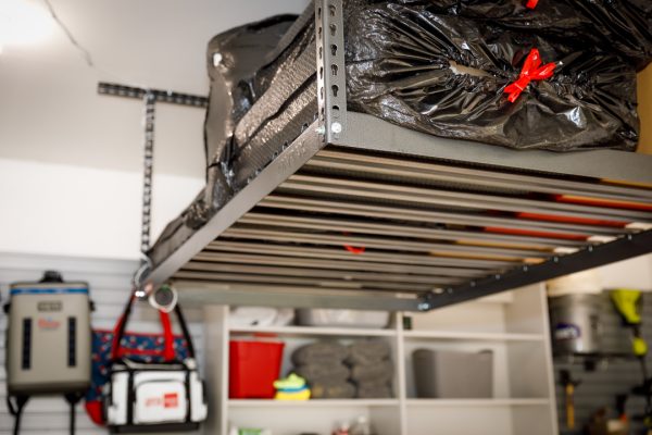 Overhead garage rack with black storage bags, items hanging on wall, and shelves below.