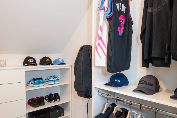 White custom closet with shelves for sneakers and hats, and hanging sports jerseys and hoodies.