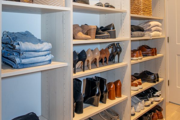 Custom closet with light wooden shelves storing clothes, shoes, and handbags.