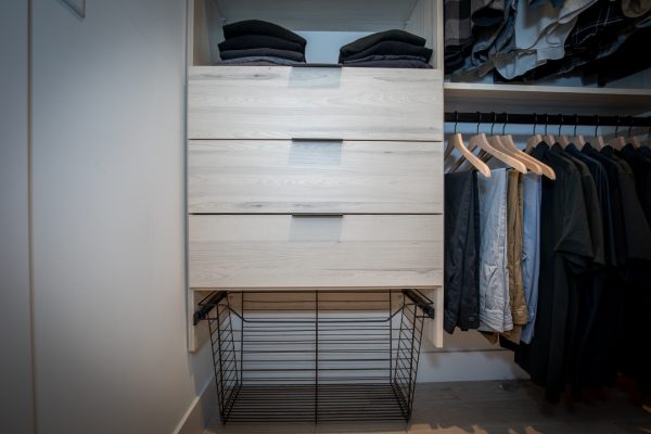 Light wood closet organizer with three drawers, folded clothes, hanging shirts, and a pull-out wire basket.