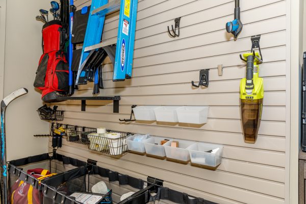 Organized garage wall with gray slatwall, showing golf clubs, a ladder, hockey stick, and vacuum.