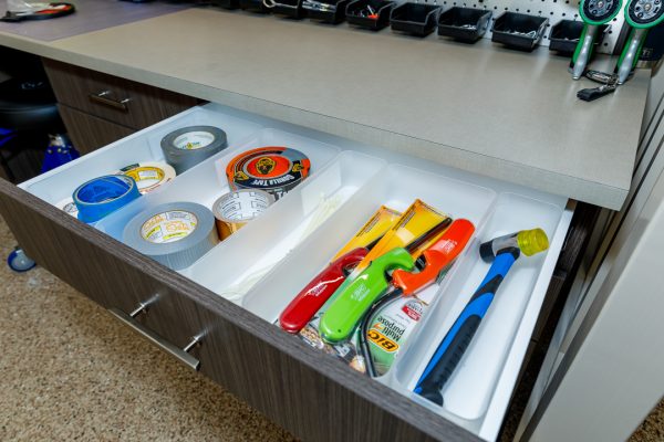Open drawer with clear organizers storing various tapes, cable ties, lighters, and a hammer.
