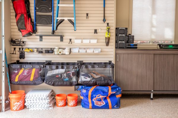 Organized garage with slatwall storage system, various items, and wood cabinets.