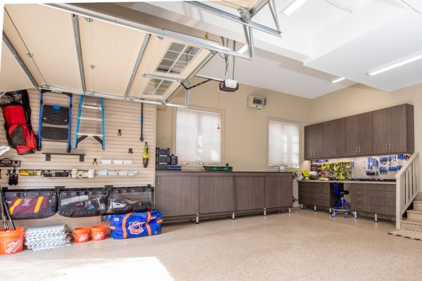 Spacious, organized garage with light beige walls, brown cabinets, storage systems, tools, and a speckled epoxy floor.