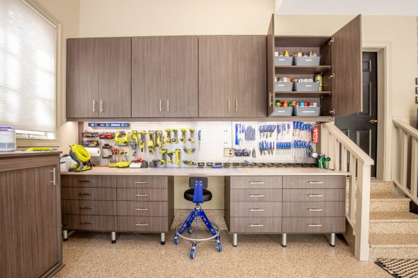 Organized garage workshop with wood-look cabinets, pegboards filled with tools, and a workbench.