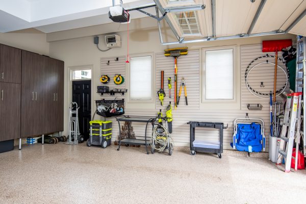 Organized garage with gray cabinets, wall-mounted tools, and clean epoxy floor.