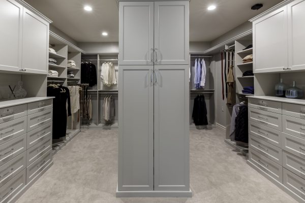 Luxurious custom walk-in closet: light gray cabinets, shelves with folded clothes, hanging shirts, dresses, ties.