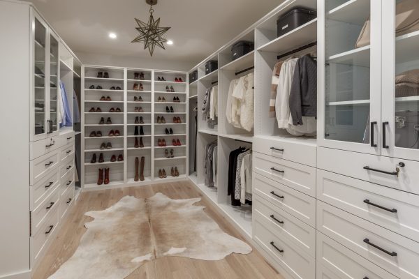 A spacious white walk-in closet with built-in shelves for shoes, hanging clothes sections, drawers, and glass-front cabinets.