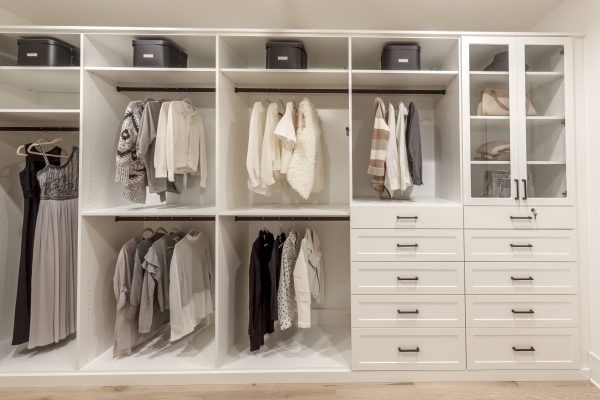 A white custom closet system with open shelving, hanging clothes, drawers, and glass-front cabinets.