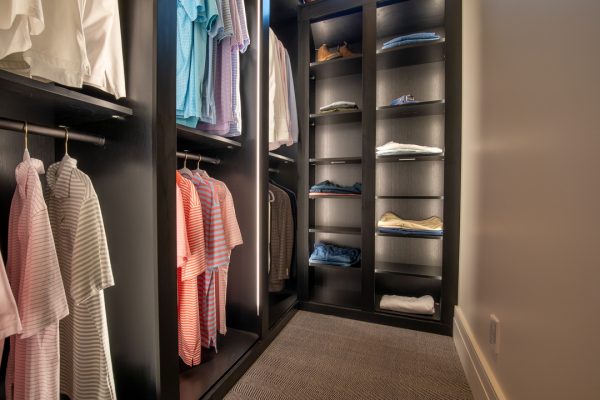 Custom closet organization system in a dark wood finish with built-in LED lighting, clothing, and folded apparel.