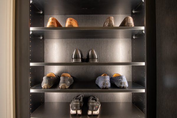A tall, dark shoe rack with multiple shelves displaying various pairs of shoes.