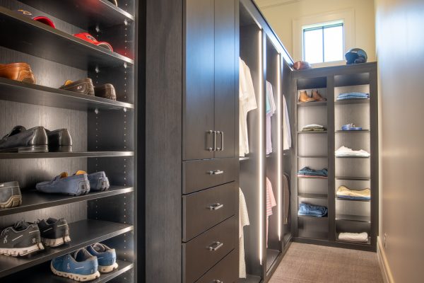 A luxurious walk-in closet with dark wood cabinetry, integrated lighting, shoe racks, drawers, and hanging clothes.