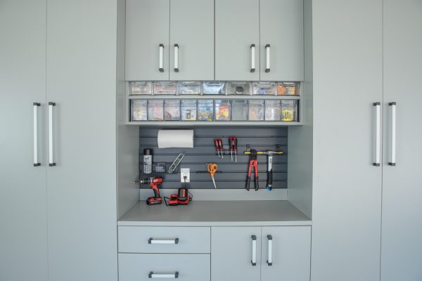 Gray garage cabinets with tools neatly organized on a slatwall and in clear bins above a countertop.