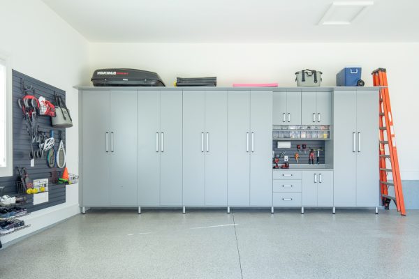 Clean, organized garage with light gray cabinets, black slatwall storage, tools, and a car-top carrier.