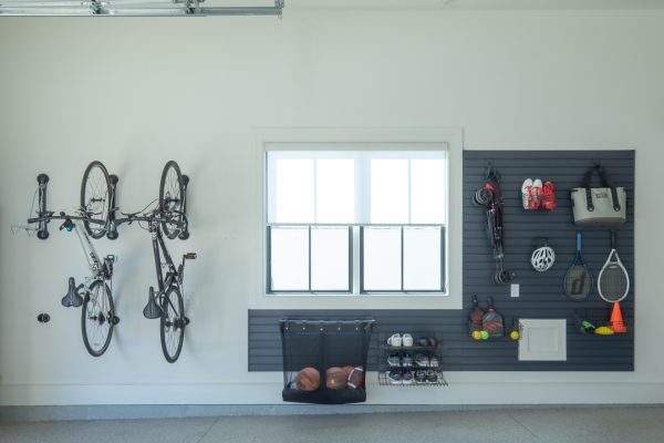 Organized garage with two bikes hanging, window, and slatwall full of sports gear, shoes, and a bag.