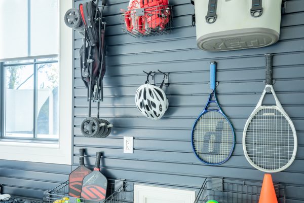 Garage wall storage with sports equipment, including a wagon, tennis rackets, and a bike helmet.