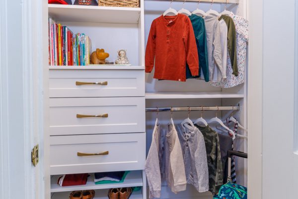 White closet with custom shelving and drawers filled with children's clothes, books, and accessories.
