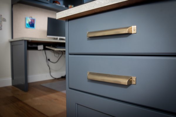 Close-up of navy blue desk drawers with gold pull handles, a gray countertop, and blurred office in the background.