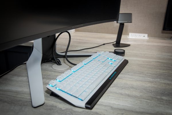 Dell Alienware white mechanical keyboard with blue RGB backlighting next to a black monitor.